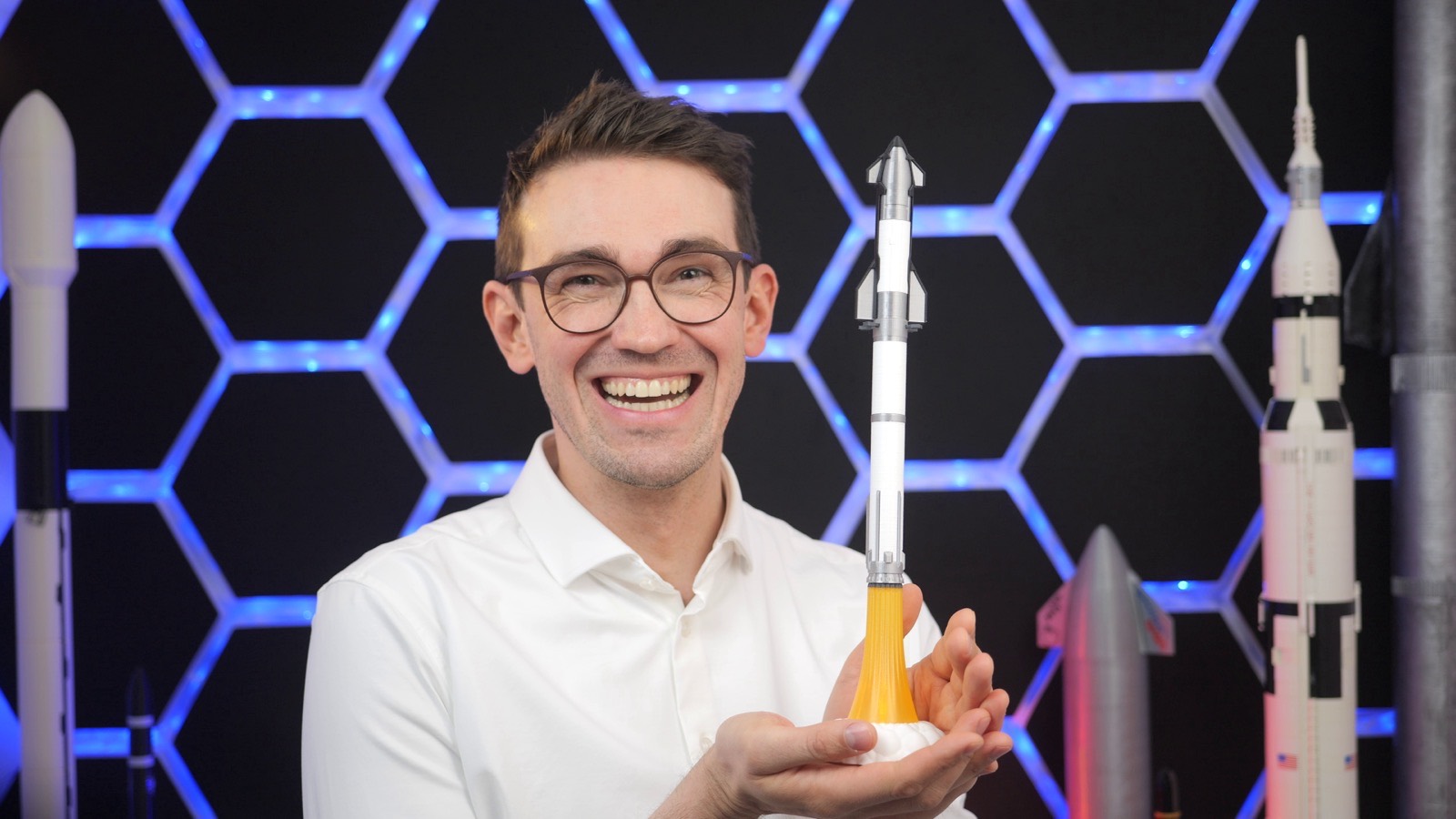 Mo hält ein Starship-Modell in der Hand, umgeben von Raketenmodellen